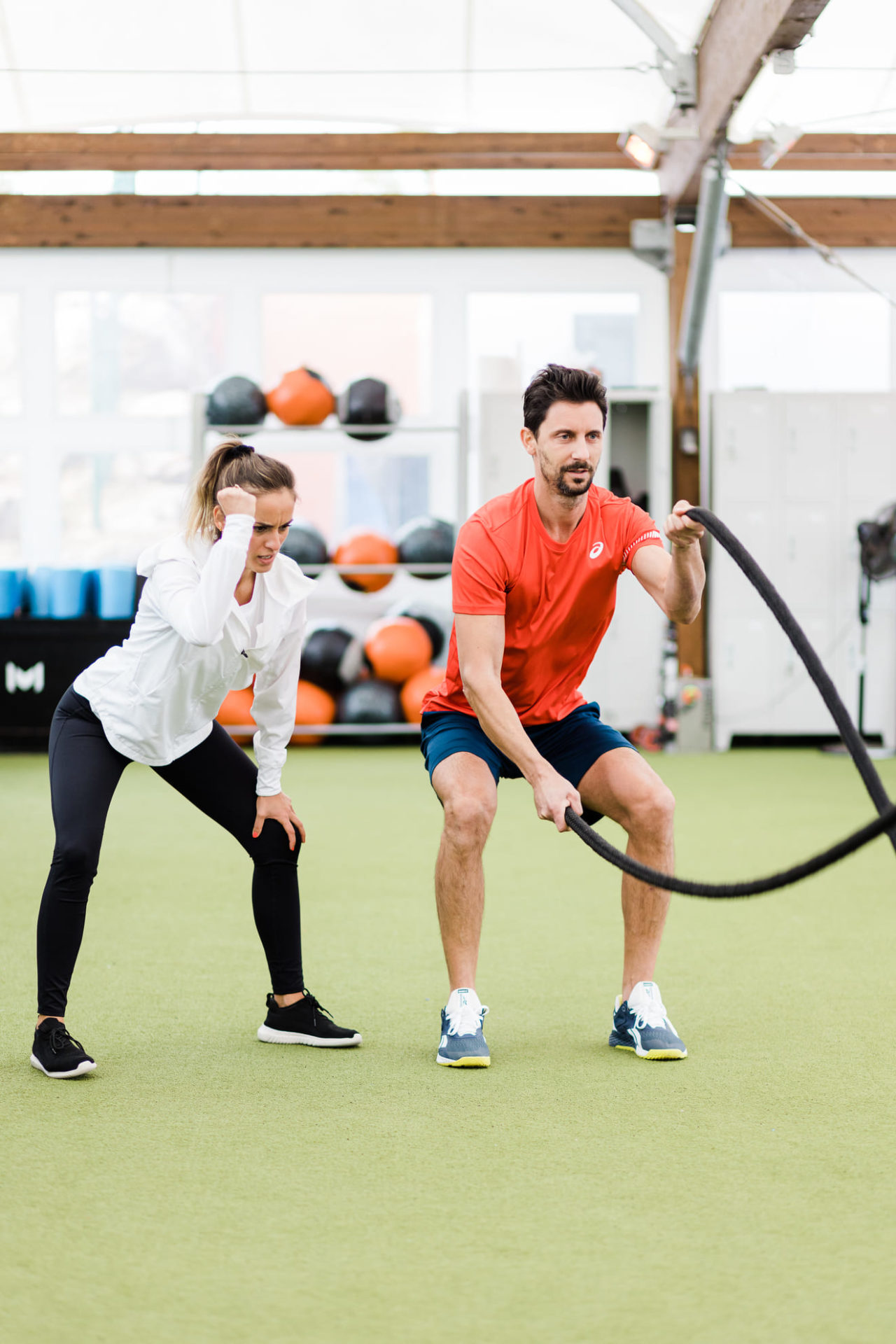 L'image montre une entraîneuse qui entraîne un homme à devenir plus fort dans une salle de musculation. L'homme fait de la corde.