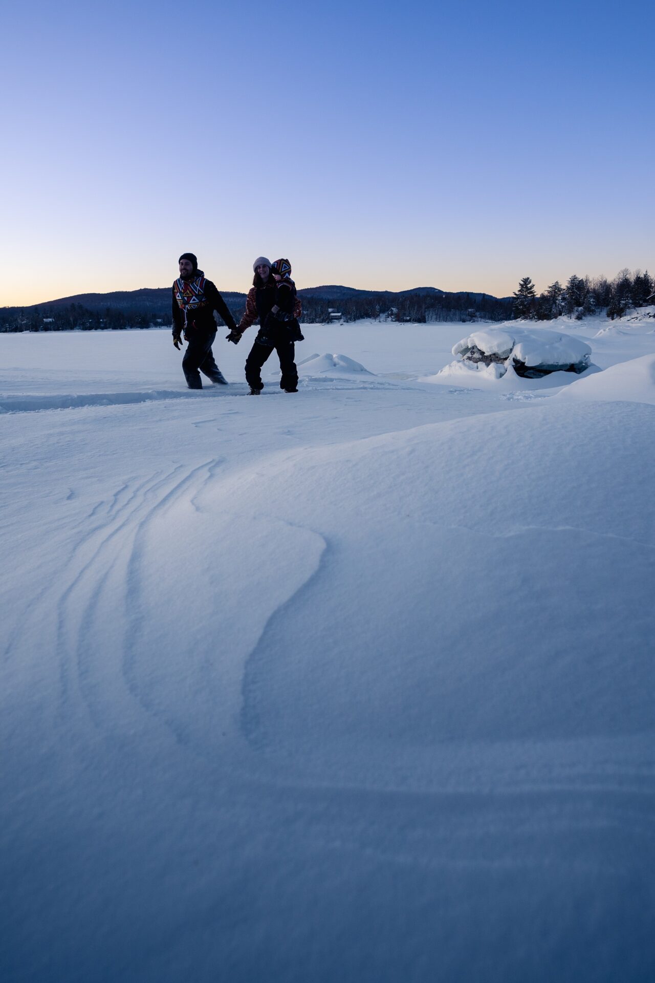 L'image montre une famille habillé en sorte qu'ils n'ont pas froid. De plus, l'image est couverte d neige avec des montagnes comme vue d'arrière.